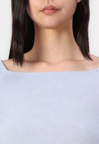 Top ribbed azul claro com decote quadrado, textura suave e detalhes de costura subtil. O design é ajustado nos ombros.
