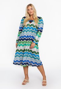 Langärmliges Kleid mit Chevron-Muster in Grüntönen, Blau und Hellgrau; verfügt über einen V-Ausschnitt und einen ausgestellten Saum.