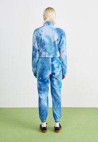 Blå tie-dye joggedress med en myk tekstur, med elastiske mansjetter og midjebånd. Designet inkluderer varierende nyanser av blått.