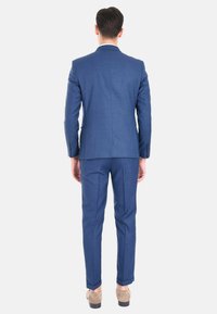 Abito sartoriale da uomo in tessuto blu scuro. Presenta un blazer a un bottone e pantaloni slim-fit. Tessuto liscio con design minimalista.