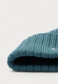 Berretto lavorato a maglia in teal, caratterizzato da una texture a coste e un risvolto. Materiale morbido con un piccolo dettaglio del logo sul lato.