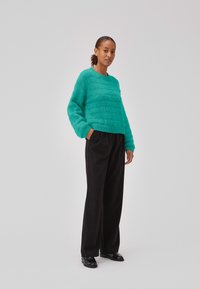 Turkusowy, strukturalny sweter typu knit z okrągłym dekoltem, połączony z czarnymi spodniami o wysokim stanie i czarnymi butami. Sweter ma luźny krój.