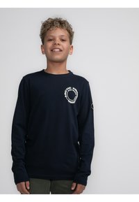 Maglietta a manica lunga blu navy in cotone, con un logo circolare sul petto e un'emblema sulla manica. Tessuto liscio, design semplice.