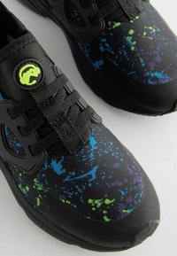 Black athletic shoe with a splatter pattern in blue, green, and purple. Features textured fabric, laces, and circular branding detail on the tongue.