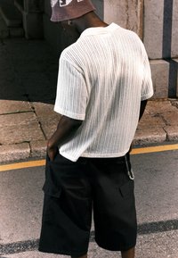 Witte geribbelde short-sleeve shirt met een relaxed fit, gecombineerd met zwarte cargo shorts met zijzakken en een kettingaccent.