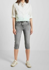 Jeans cortos grises con un corte recto y textura desgastada, combinados con una camisa de manga larga abotonada de color verde degradado a blanco.