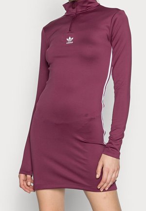 Bordowa obcisła sukienka Adidas z długim rękawem, białymi bocznymi paskami i kołnierzem z zamkiem na ćwiartkę, noszona na tułowiu i górnej części nóg.