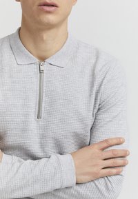 Helles graues Langarm-Polohemd mit strukturiertem Design, ausgestattet mit einem Reißverschluss und einem klassischen Kragen. Weicher Stoff mit gerippten Bündchen.