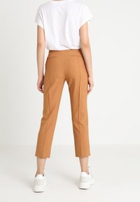 Brown tailored cropped trousers with back pockets, featuring a smooth texture. Paired with a white short-sleeve shirt and white sneakers.