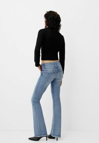 Široke kavbojke v svetlo modri barvi z zbledelim učinkom, pet žepov in črne visokotlačne čevlje. Črni rebrasti skrajšani pulover.