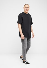 Must olla oversized must t-särk lühikeste varrukatega, millele on paari pandud kulunud hallid teksad ja mustad tossud, millel on valged aktsendid ja shoelaces.