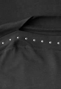 Un tissu noir à texture lisse présente une rangée de huit petits strass argentés le long de l'encolure. Design simple et discret.