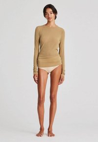 Beige Langarmshirt aus weichem Material, taillierter Schnitt mit Rundhalsausschnitt; kombiniert mit hellbeigen Boyshorts, barfuß.