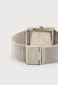 Ανδρικό ρολόι Guess από ανοξείδωτο ατσάλι με ορθογώνια κάσα, μπρασελέ από πλέγμα και κούμπωμα, που δείχνει την πίσω πλευρά του ρολογιού με χαραγμένες τις λεπτομέρειες της μάρκας.