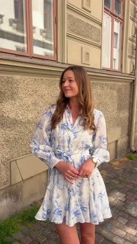 Blomstrete kjole med blå og hvit akvarellmønster, lange ermer, knappet foran, innsvinget midje og bredt utslag. Silkeaktig tekstur.