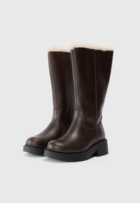 Bottes en cuir marron hautes jusqu'au genou, avec une doublure en fausse fourrure crème douce, un bout arrondi et une semelle plateforme noire avec des détails de couture.