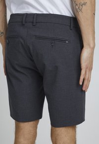 Mørkegrå tilpassede shorts med en glatt tekstur, som har to baklommer med knapper og subtile sømdetaljer.