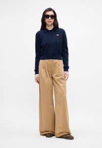 Námornícky strihaný sveter s golierom a tromi gombíkmi, spárovaný s voľnými béžovými nohavicami a slip-on topánkami s leopardím vzorom.