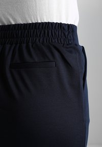 Marinblå joggers med elastisk midjeband, som har en liten, platt ficka. Tyget verkar mjukt med en slät yta.