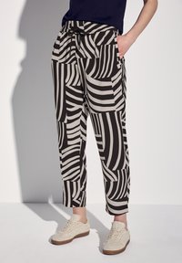 Pantalon à motifs noir et blanc avec une taille élastique et des poches latérales, présentant des motifs de rayures audacieux variés. Une paire de baskets crèmes texturées.
