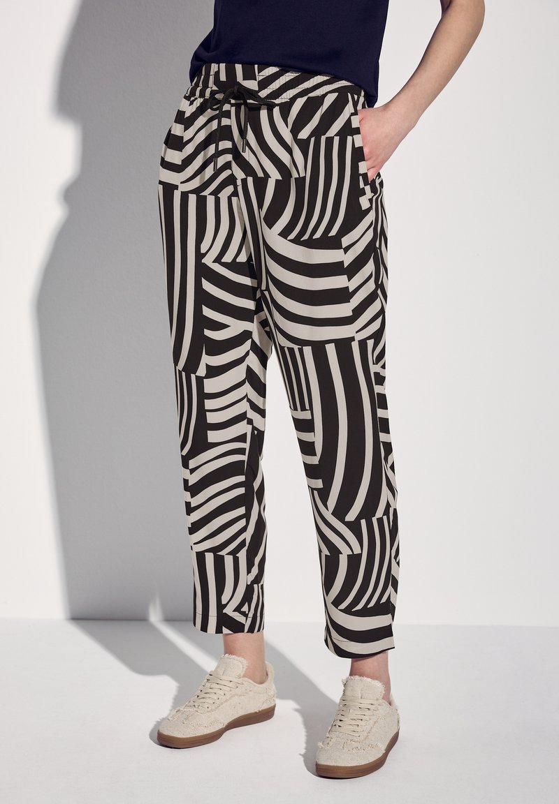 Pantalon à motifs noir et blanc avec une taille élastique et des poches latérales, présentant des motifs de rayures audacieux variés. Une paire de baskets crèmes texturées.