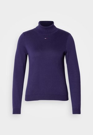 Violeta turtlenecka džemperis, izgatavots no gluda, elastīga auduma. Tam ir garas piedurknes un ribota apakšmala, ar nelielu trīsgkrāsu logo uz krūtīm.