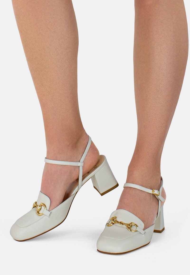 Scarpe slingback in pelle bianca con punta quadrata e tacco medio. Presentano un accessorio a catena dorata sulla parte anteriore e una cinghia alla caviglia.
