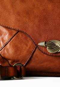 Bolso de cuero marrón con una superficie texturizada, que presenta un cierre de bronce trenzado y costuras detalladas a lo largo de los bordes.