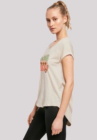 Beige t-shirt gemaakt van zachte stof, met een afbeelding van een vintage bus omringd door groene bomen en bloemen. Korte mouwen en een ronde halslijn.