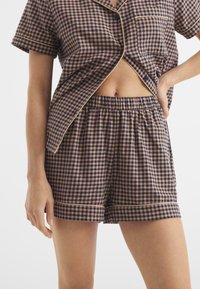 Conjunto de dos piezas con estampado de cuadros, que incluye una blusa de botones con un bolsillo y pantalones cortos con cintura elástica, en tonos azul marino y rosa empolvado.