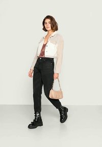 Jaqueta de denim cropped em bege claro e branco, blusa padrão em bordeaux, jeans pretos de cintura alta e botas chunky pretas com atacadores, segurando uma pequena bolsa bege.