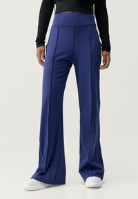 Mörkblå utsvängda byxor i stretchigt material, med hög midja och vertikala sömmar, stylade med vita sneakers.