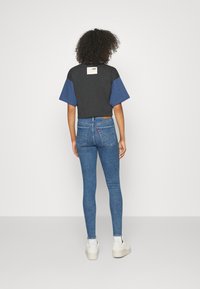 Camiseta recortada en color negro y azul con bloques de color, combinada con jeans ajustados azul denim y zapatillas blancas, que presenta una etiqueta de logo en la camiseta.