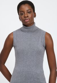 Maglione grigio senza maniche con collo alto realizzato in morbido tessuto a maglia, caratterizzato da un collo a coste e un design aderente che mette in risalto la silhouette.