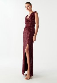 Burgundia sädelev õhtukleit sügava V-kaeluse, ilma varrukateta disaini, taljesse jäänud silueti ja reie kõrguse lõikega; omab elegantset sädelust ja tekstuuri.