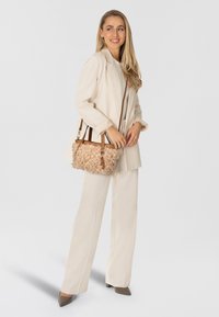 Blazer y pantalones color crema con un bolso texturado beige que presenta acentos ondulados y correas de cuero marrón, todo sobre un fondo claro.