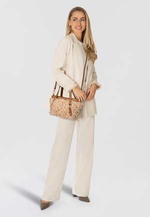 Blazer y pantalones color crema con un bolso texturado beige que presenta acentos ondulados y correas de cuero marrón, todo sobre un fondo claro.