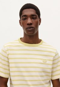 Stribet bomulds t-shirt i lys grøn og off-white, med rund hals og et lille logo-patch på brystet. Blød tekstur.
