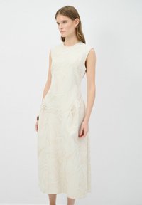 Mouwloze midi-jurken in lichtbeige met een subtiel bladdessin, voorzien van zijzakken en een vloeiende siloeet. Huidige, textuurstof.