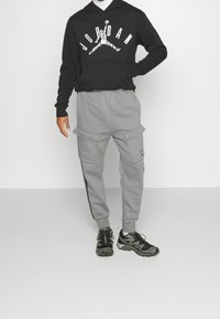 Svart huvtröja med "JORDAN" grafisk design, ihop med grå cargobyxor med två sidofickor och svarta detaljer; bärs med svarta sneakers.