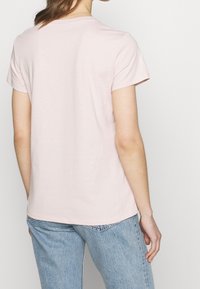 Kortärmad, rosa bomullströja med rund halsringning, något sviktande nederkant, som bärs med ljusblå denimjeans. Slät textur.