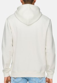 Haut à capuche blanc en tissu doux, avec une grande capuche, des poignets côtelés et une coupe décontractée. Le dos présente un design lisse et sans embellissement.