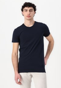 Navyblaues T-Shirt mit kurzen Ärmeln aus Baumwollstoff, mit Rundhalsausschnitt. Die Passform ist slim, wodurch der Oberkörper betont wird. Glatte Textur, minimalistisches Design.