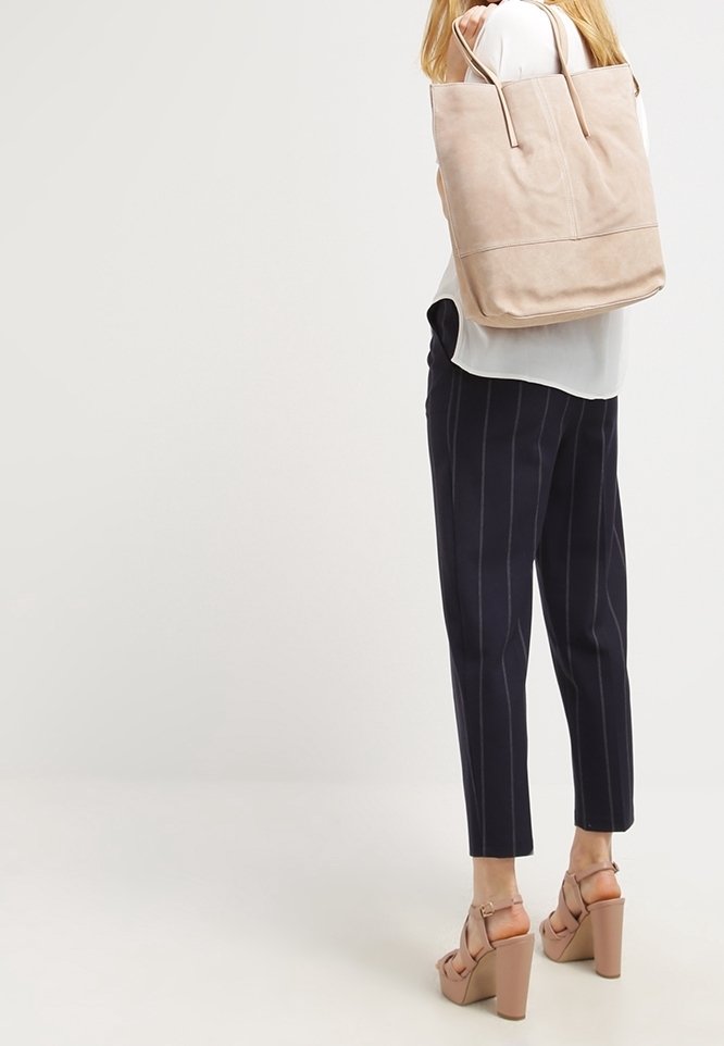 Sac fourre-tout en cuir beige avec deux longues anses, design minimaliste, texture lisse et fond plat. Assorti à un pantalon rayé bleu marine.