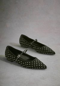 Ballerine in suede nero con punta affusolata, decorate con pois bianchi. Presentano una sottile cinghia con una fibbia decorativa e un tacco basso.