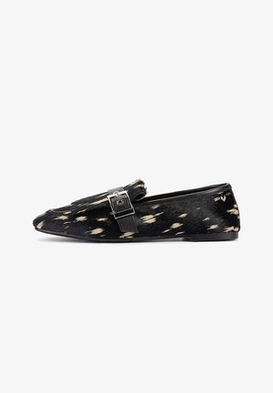 Zapato tipo mocasín plano con manchas negras y blancas, hebilla plateada en la parte superior, tacón bajo y puntera puntiaguda, mostrado de lado sobre un fondo blanco.