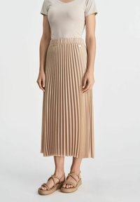 Beżowa plisowana midi spódnica z elastycznym paskiem, g�ładką teksturą i subtelnym połyskiem. Zestawiona z cielistymi sandałami na paski.