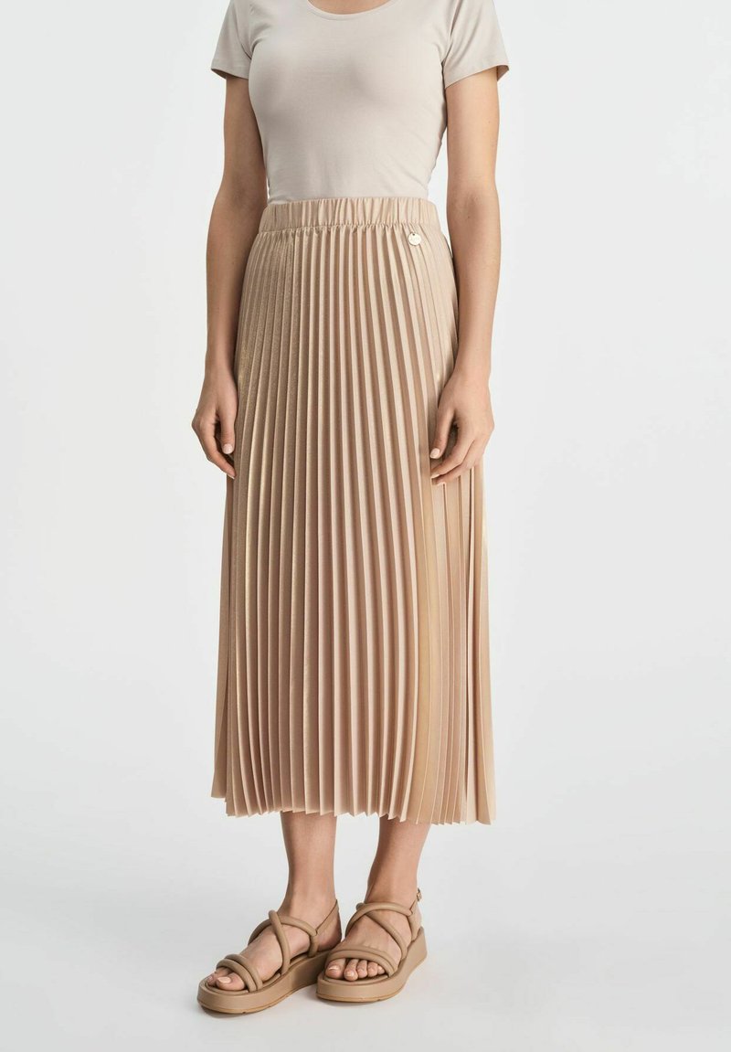 Beżowa plisowana midi spódnica z elastycznym paskiem, gładką teksturą i subtelnym połyskiem. Zestawiona z cielistymi sandałami na paski.