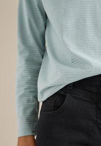 Hellblaues Langarmoberteil mit horizontalen Streifen, kombiniert mit schwarzen Jeans, die über eine vordere Tasche und eine enganliegende Silhouette verfügen.