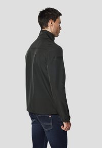 Giacca softshell nera con collo alto, silhouette aderente e texture liscia. Presenta dettagli con logo sulla spalla e polsini con zip.